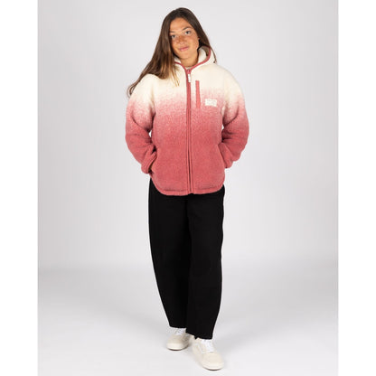 A woman wearing a Saltrock full zip hooded Alba sherpa fleece in a dip dye cream to pink design with black trousers.