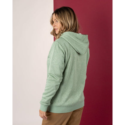 Woman wearing a green Saltrock hoodie standing against a red and white wall.