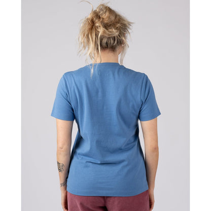 Back view of a woman wearing a Saltrock short sleeve Trader Daze t-shirt in bright blue with burgundy trousers on a plain background