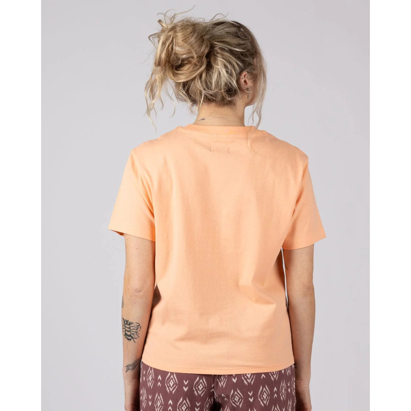 Back view of a woman wearing a Saltrock short sleeve Trader Daze t-shirt in peach, with a knot tie hem.