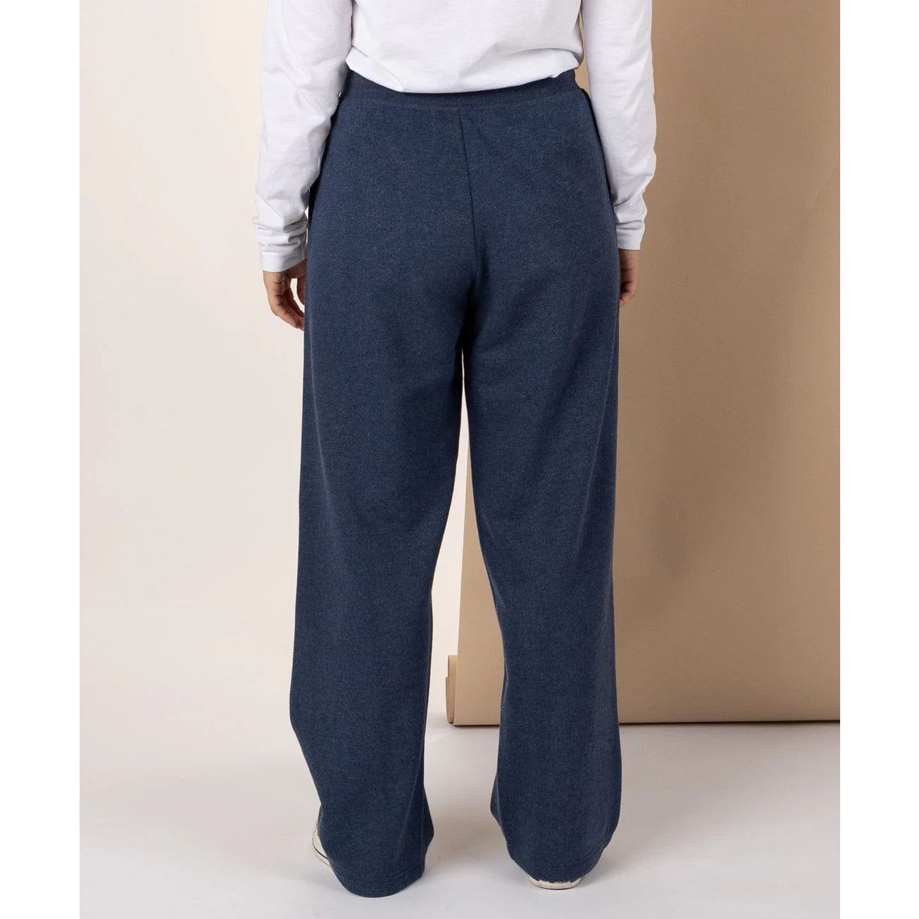 Woman wearing Saltrock Velator sweat trousers in blue marl and a white shirt against a beige background