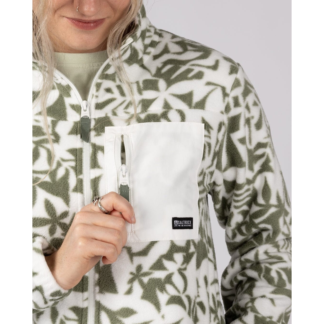 Woman wearing a green floral patterned Saltrock Balance fleece with chest zip pocket.