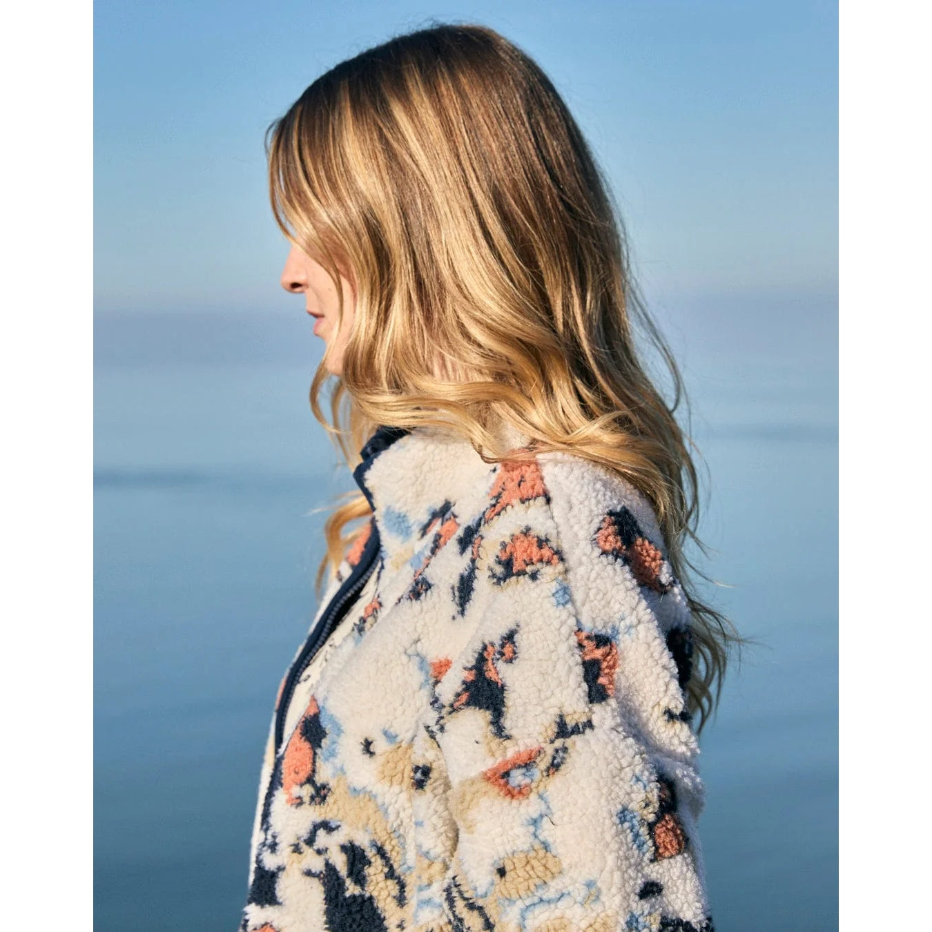 Woman wearing a patterned Saltrock Folie fleece with a blurred ocean background