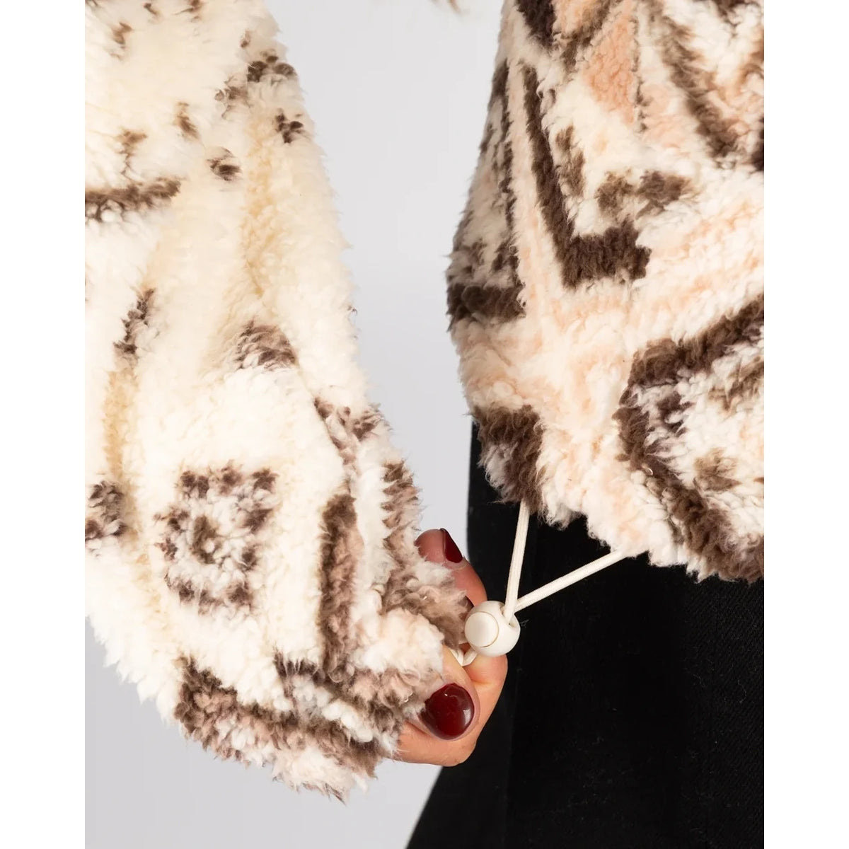Close-up view of the elastic drawcord bottom hem of a Saltrock 1/4 zip Skylar fleece in cream with a brown geometric pattern