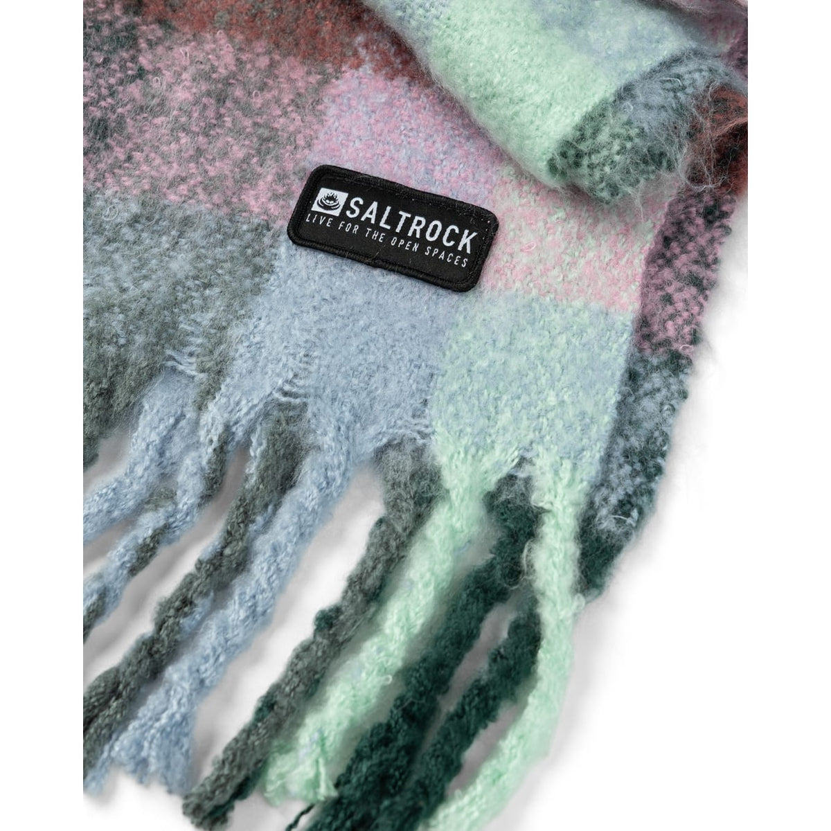 Close-up view of the tassels and logo patch, on a Saltrock womens Harvest scarf in a green and multicolour check pattern.