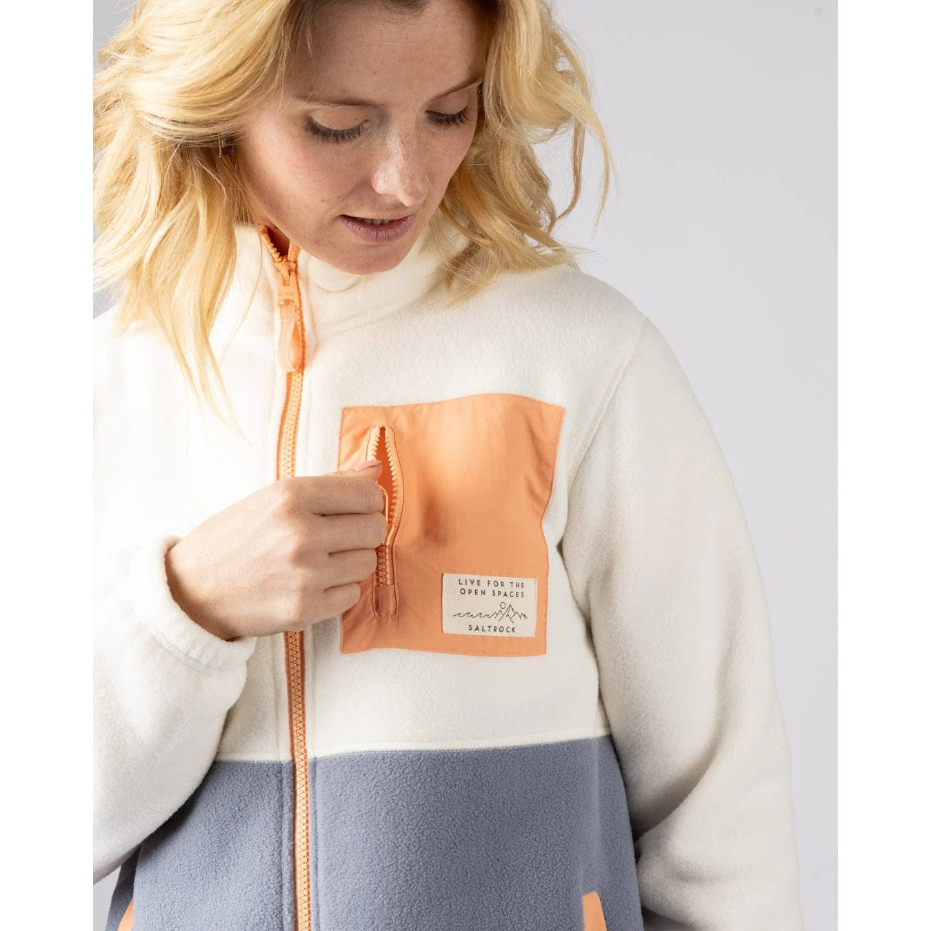 Woman wearing a Saltrock Denya colour-block full zip fleece in cream and blue with a coral chest pocket with logo patch
