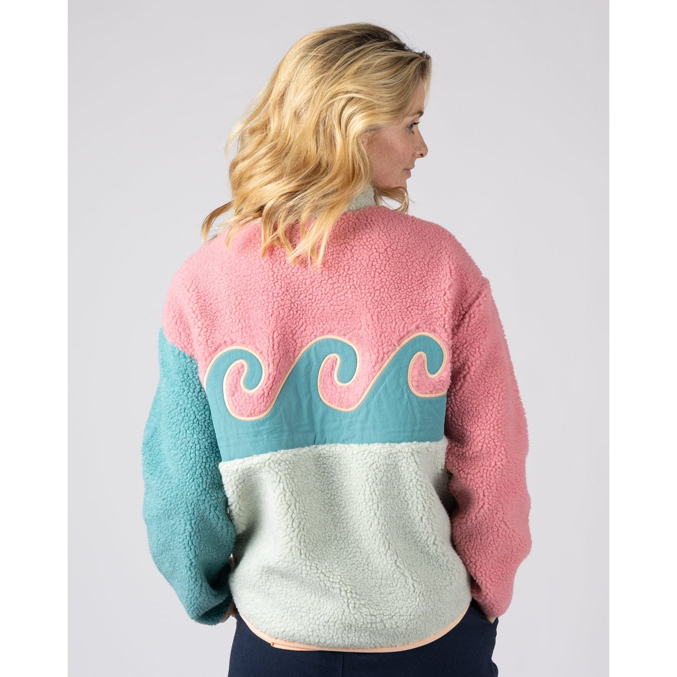 Back view of a woman wearing a colourful Saltrock Emery Wave fleece in pink, turquoise and teal