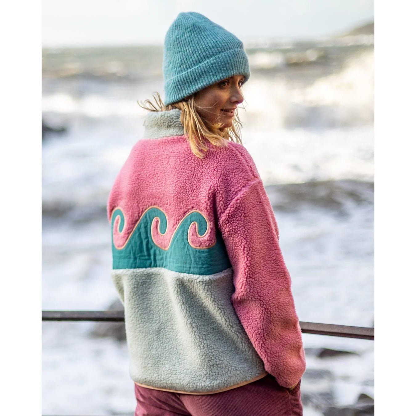 Back view of a woman wearing a Saltrock Emery Wave colour block fleece in pink and turquoise with a wave design