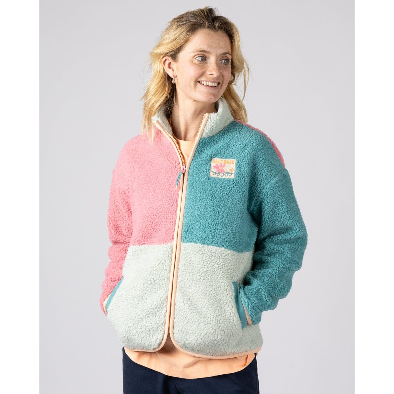 Front view of a woman wearing a Saltrock Emery Wave fleece in pink, turquoise and teal with tummy pockets