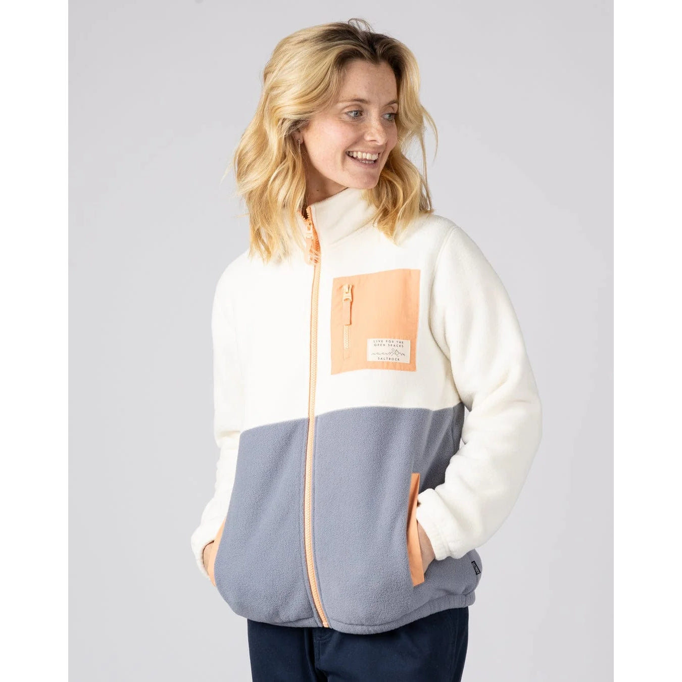 Woman wearing a Saltrock Denya full zip fleece jacket in cream, blue and coral with a chest pocket on a plain background