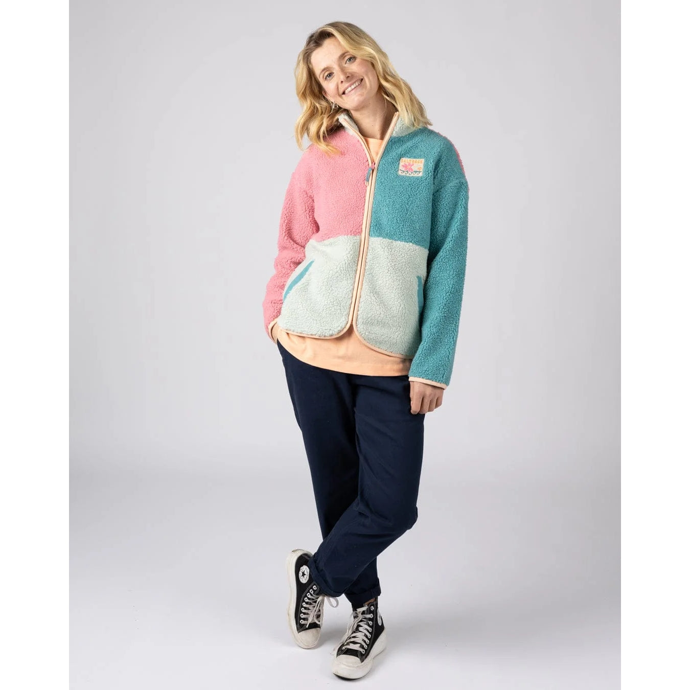 Woman wearing a Saltrock Emery Wave fleece jacket in pink, teal and turquoise with navy pants
