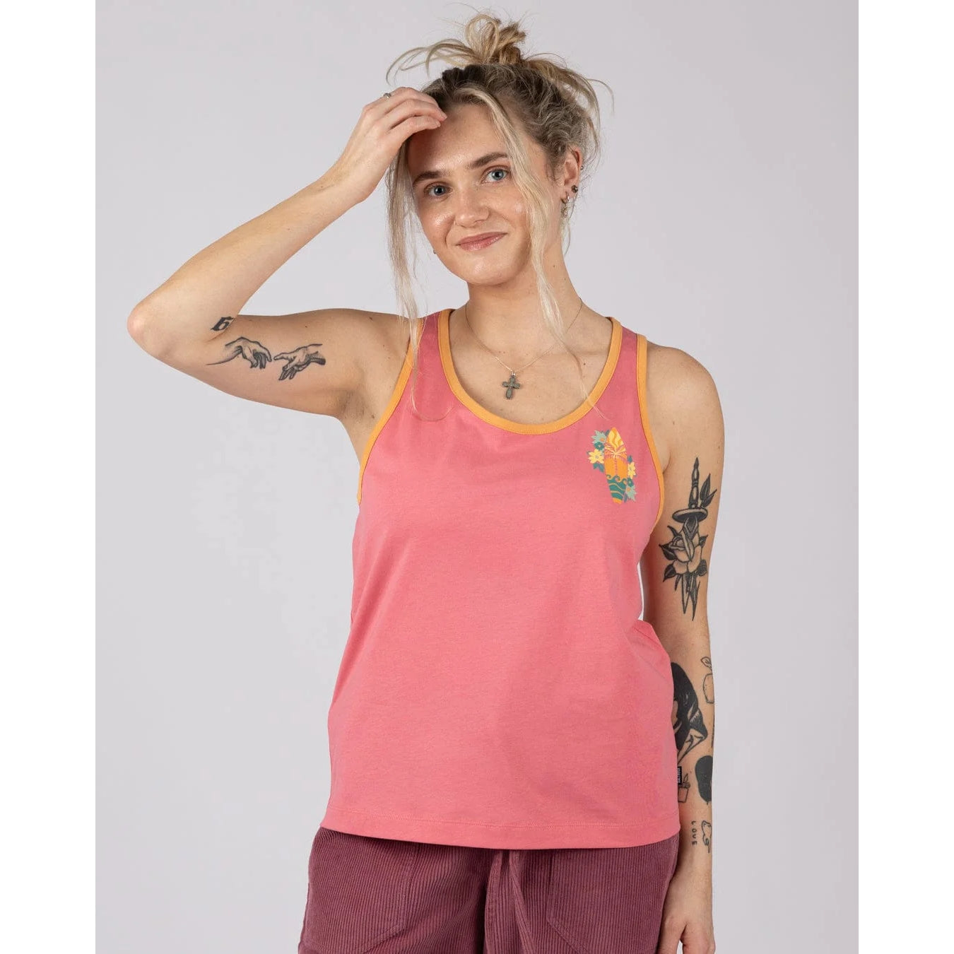 Front view of a woman wearing a pink Saltrock Sun Surfer vest top with floral surfboard print on a plain background
