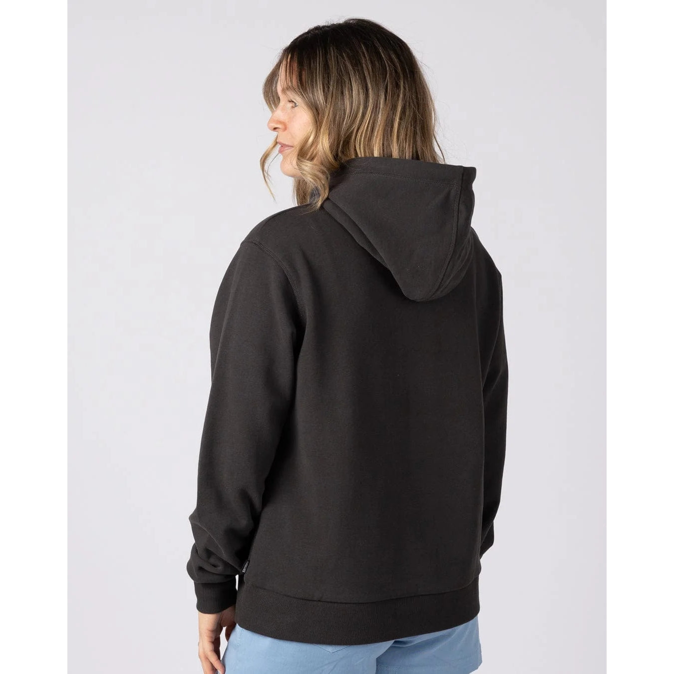 Back view of a woman wearing a Saltrock Golden Hour dark grey pop hoodie on a light grey background