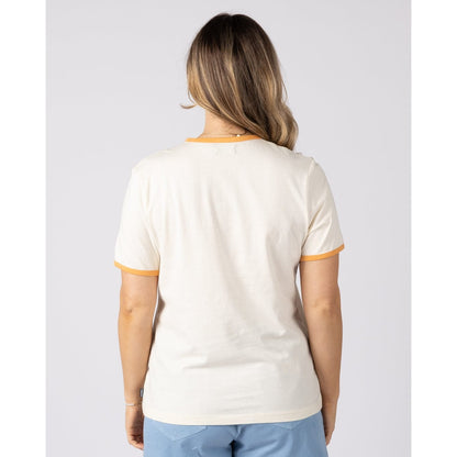 Back view of a woman wearing a Saltrock short sleeve cream Golden Hour t-shirt in orange trim and blue shorts on a plain background