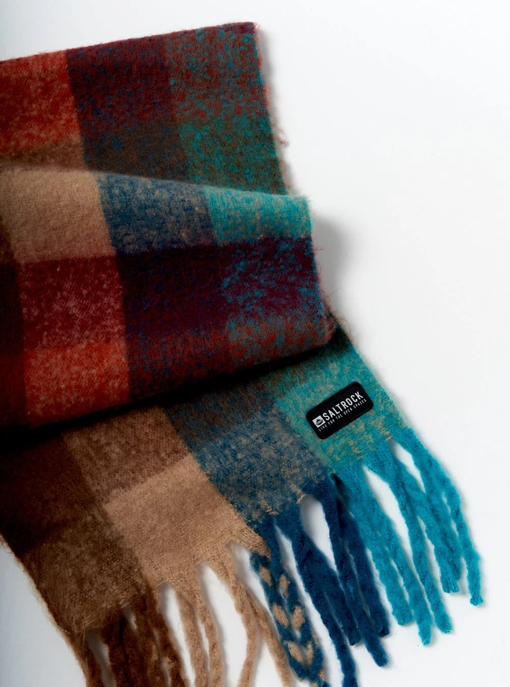 Close up of a Saltrock check pattern Harvest scarf with tassels and logo patch on a white background.