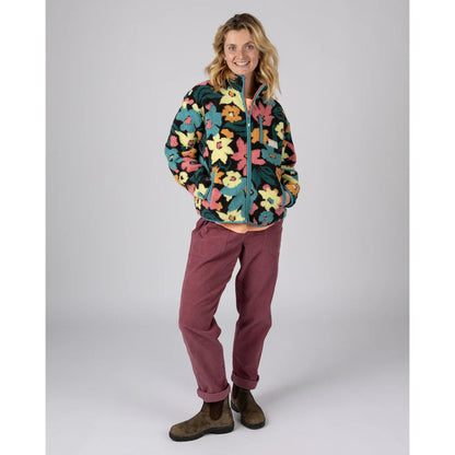 A woman wearing a multicolour floral Saltrock Holidaze zip fleece with dark pink trousers and boots