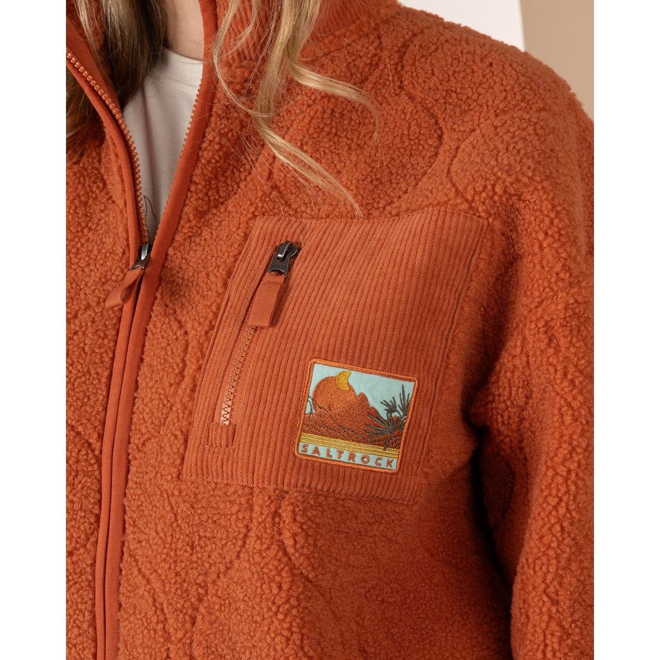 Saltrock womens orange Jarvis fleece jacket with a patch and zip pocket on the chest against a white background