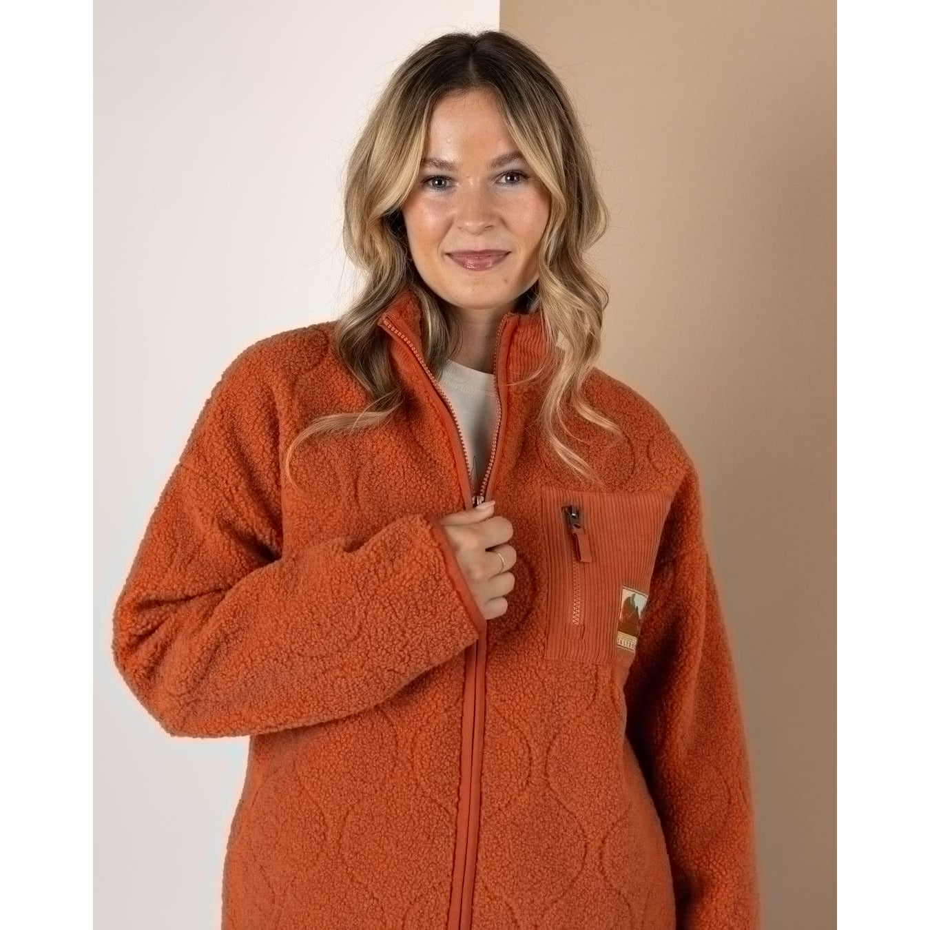 Woman wearing an orange Saltrock Jarvis fleece jacket against a neutral background