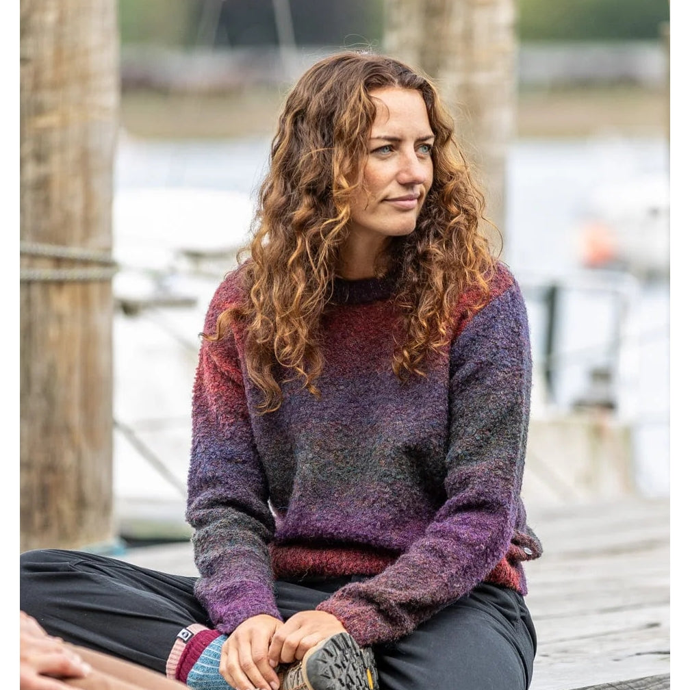 Woman wearing a Saltrock Bowden purple gradient knitted jumper sitting on a dock by a body of water.