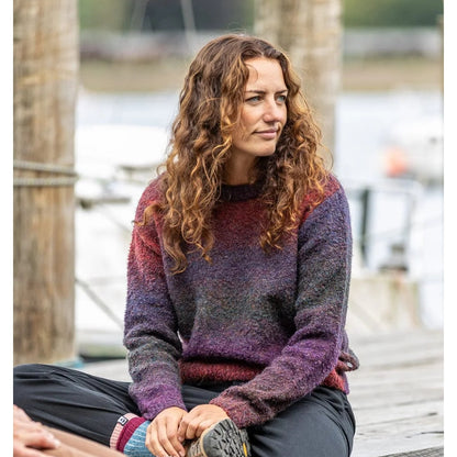 Woman wearing a Saltrock Bowden purple gradient knitted jumper sitting on a dock by a body of water.