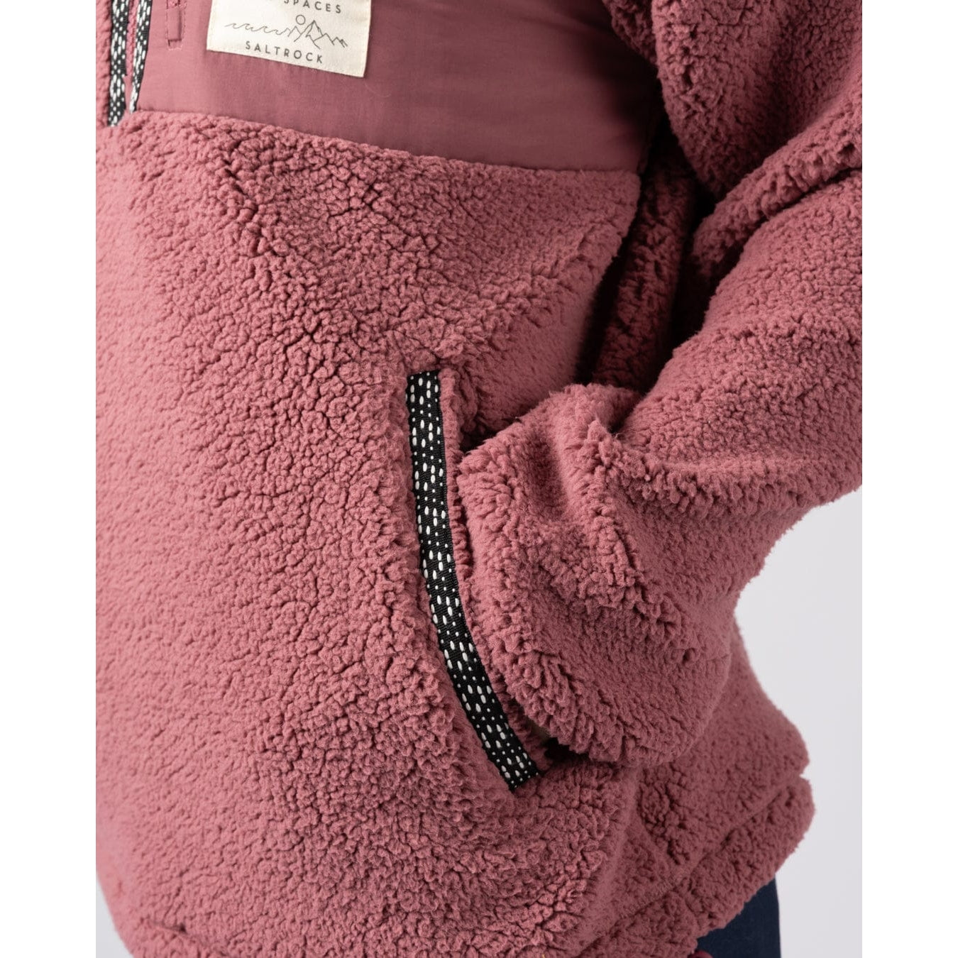 Close-up of a dark pink Saltrock Lya fleece with a brand label and tummy pocket on a white background