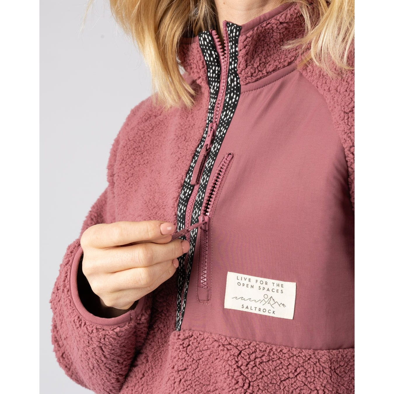 Close-up of a woman wearing a dark pink Saltrock Lya fleece with a brand label on a light grey background