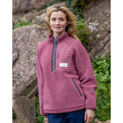 Woman wearing a dark pink Saltrock Lya fleece standing outdoors with rocks and greenery in the background