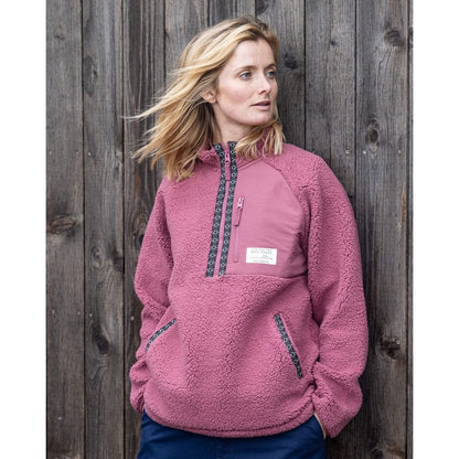 Woman wearing a dark pink Saltrock Lya 1/4 zip pullover fleece against a wooden background