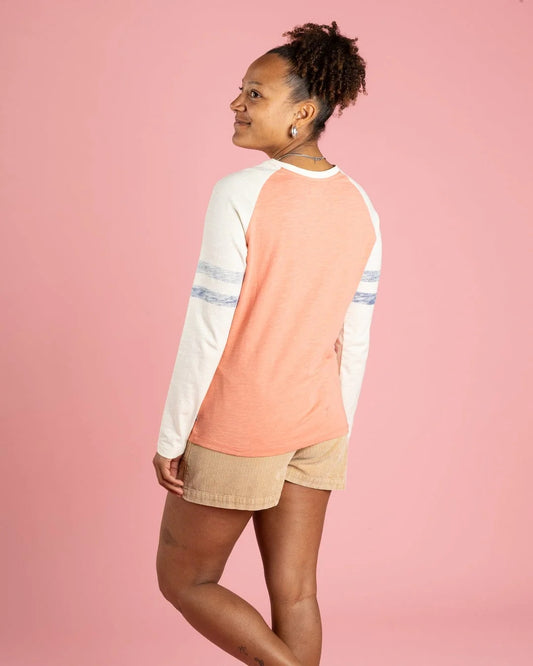 Woman wearing a coral and cream long-sleeve shirt with beige shorts on a pink background