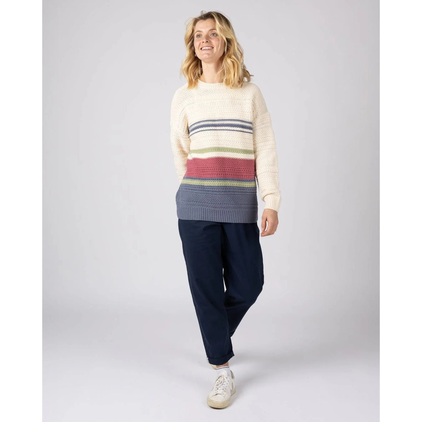 Woman wearing a Saltrock knitted stripe Sable jumper in cream with a multicolour stripe pattern and navy pants