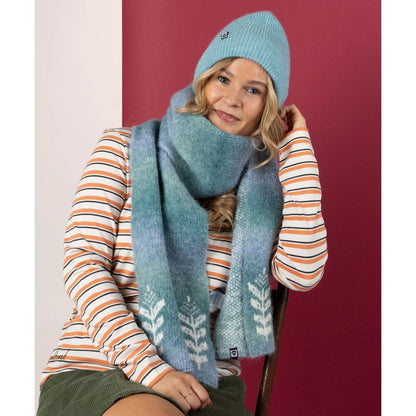 Woman wearing a Saltrock blue knit hat and scarf with a striped sweater against a red background