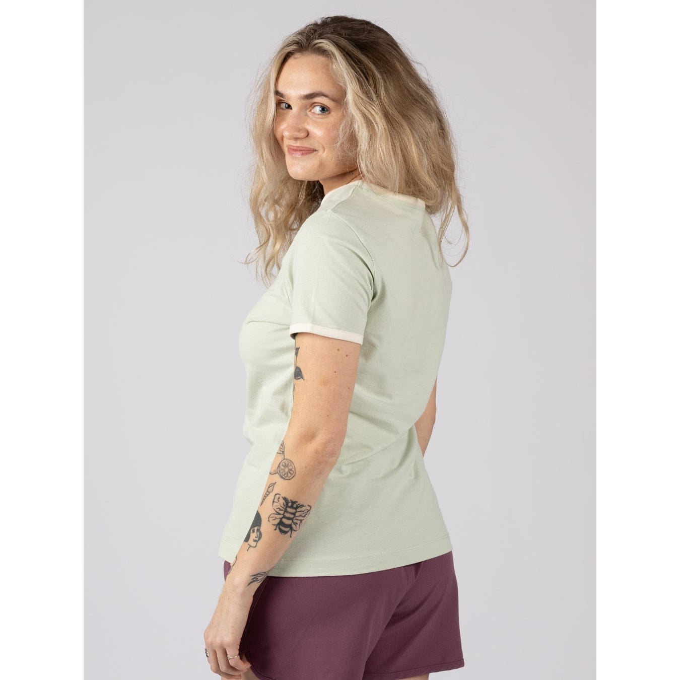 Side view of a woman wearing Saltrock a light green Golden Hour short sleeve t-shirt with sunset and sea print across the chest with burgundy shorts against a plain background