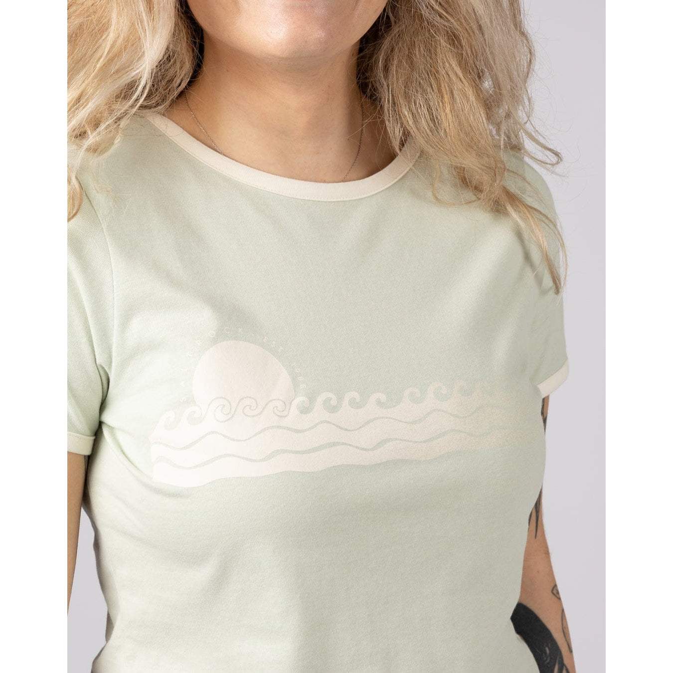 Close-up view of a woman wearing a Saltrock Golden Hour t-shirt with sunset and sea print on the chest.