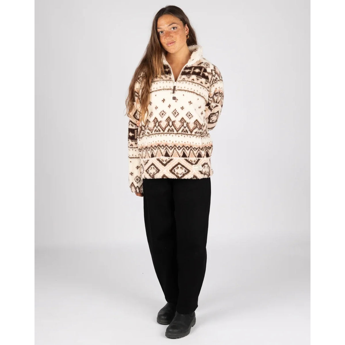 Woman wearing a Saltrock 1/4 zip Skylar fleece in cream with a brown geometric pattern and black trousers