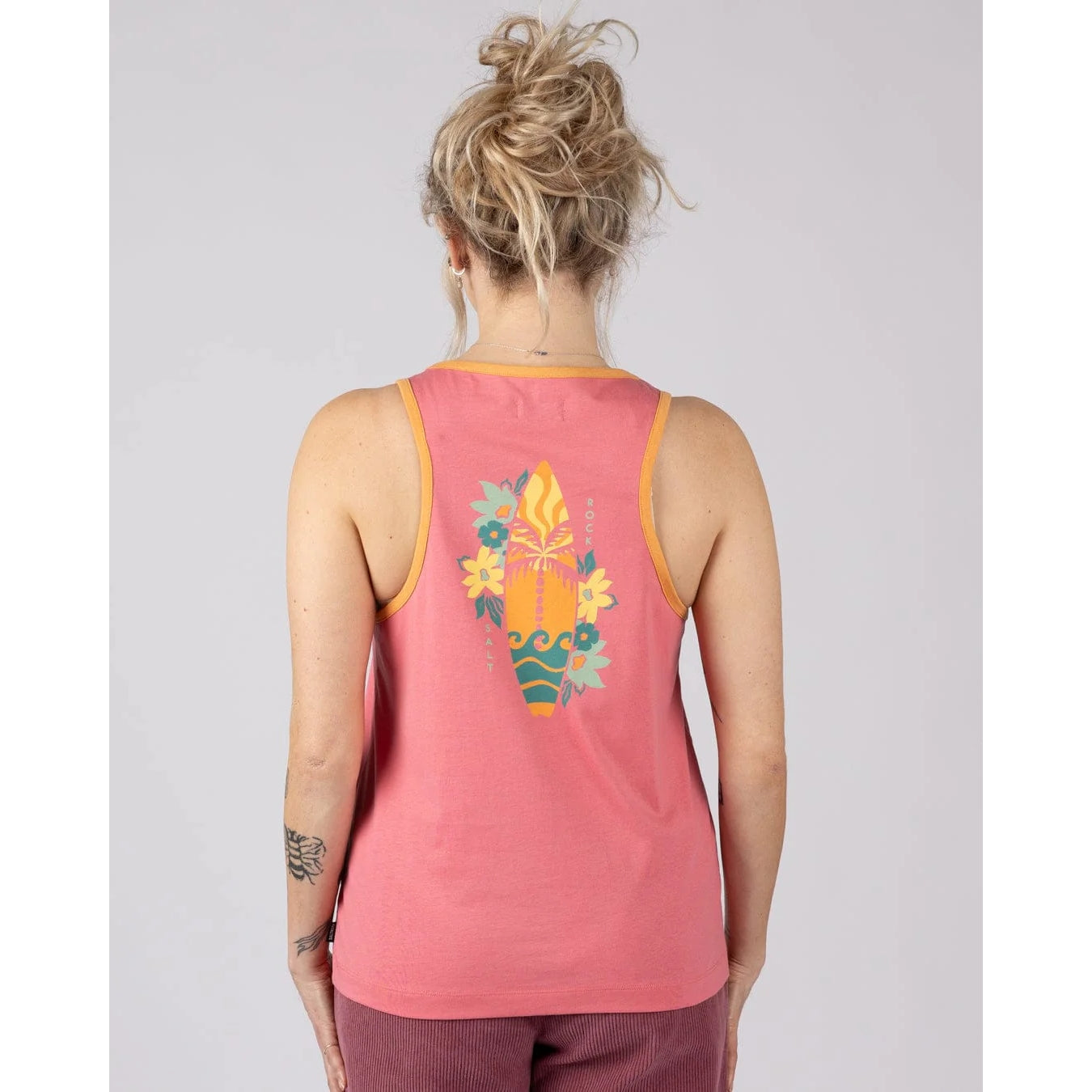 Back view of a woman wearing a pink Saltrock Sun Surfer vest top with a floral surfboard design on the back against a plain background