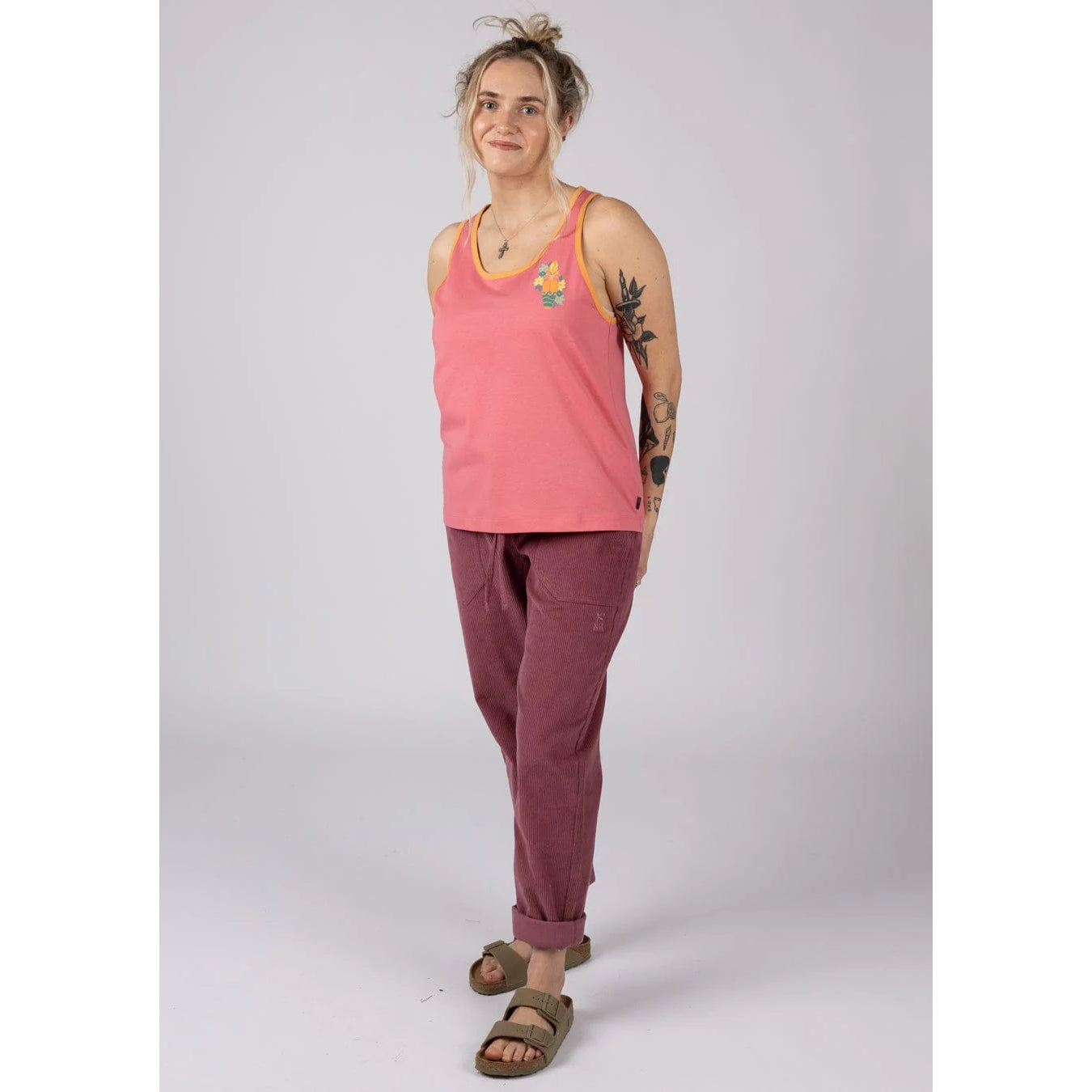 Woman wearing a bright pink Saltrock Sun Surfer vest top and maroon pants on a white background