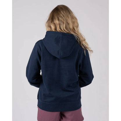 Back view of a woman wearing a navy blue Trader Daze hoodie on a light grey background