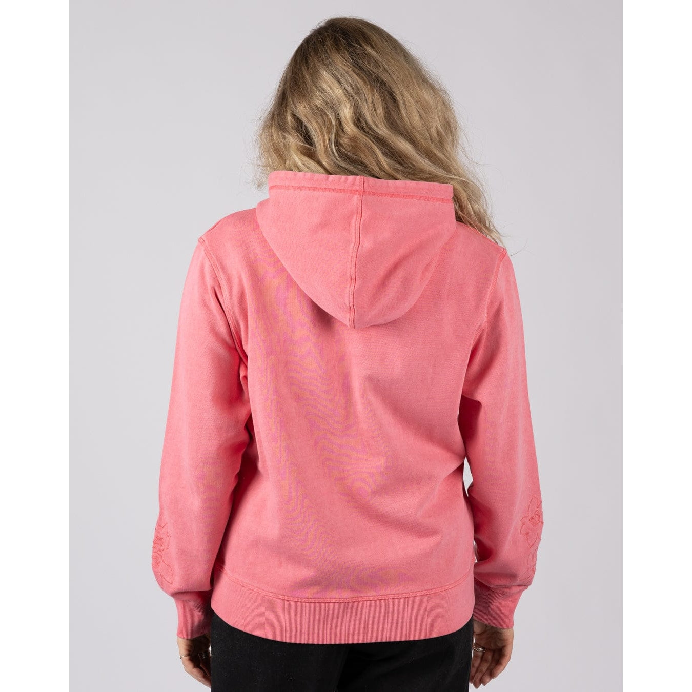 Back view of a woman wearing a bright pink Saltrock Trader Tonal pop hoodie on a plain background