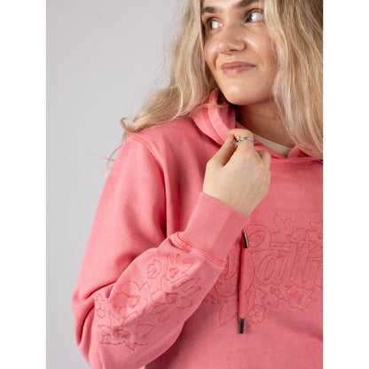 Close-up view of a woman wearing a bright pink Saltrock Trader Tonal hoodie with floral sleeve embroidery on a plain background