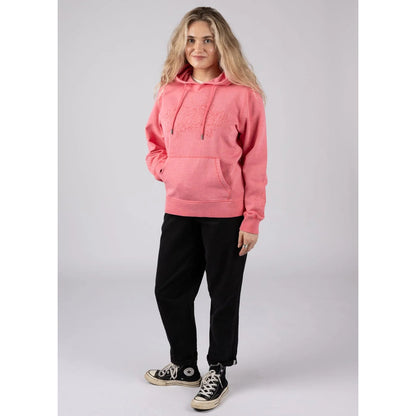 Woman wearing a Saltrock bright pink Trader Tonal pop hoodie and black pants with a white background