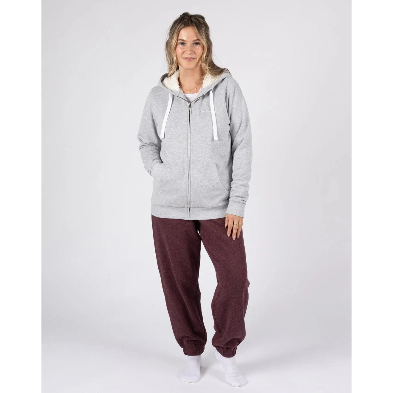Woman wearing a Saltrock full zip borg lined grey Velator hoodie and maroon trousers on a white background