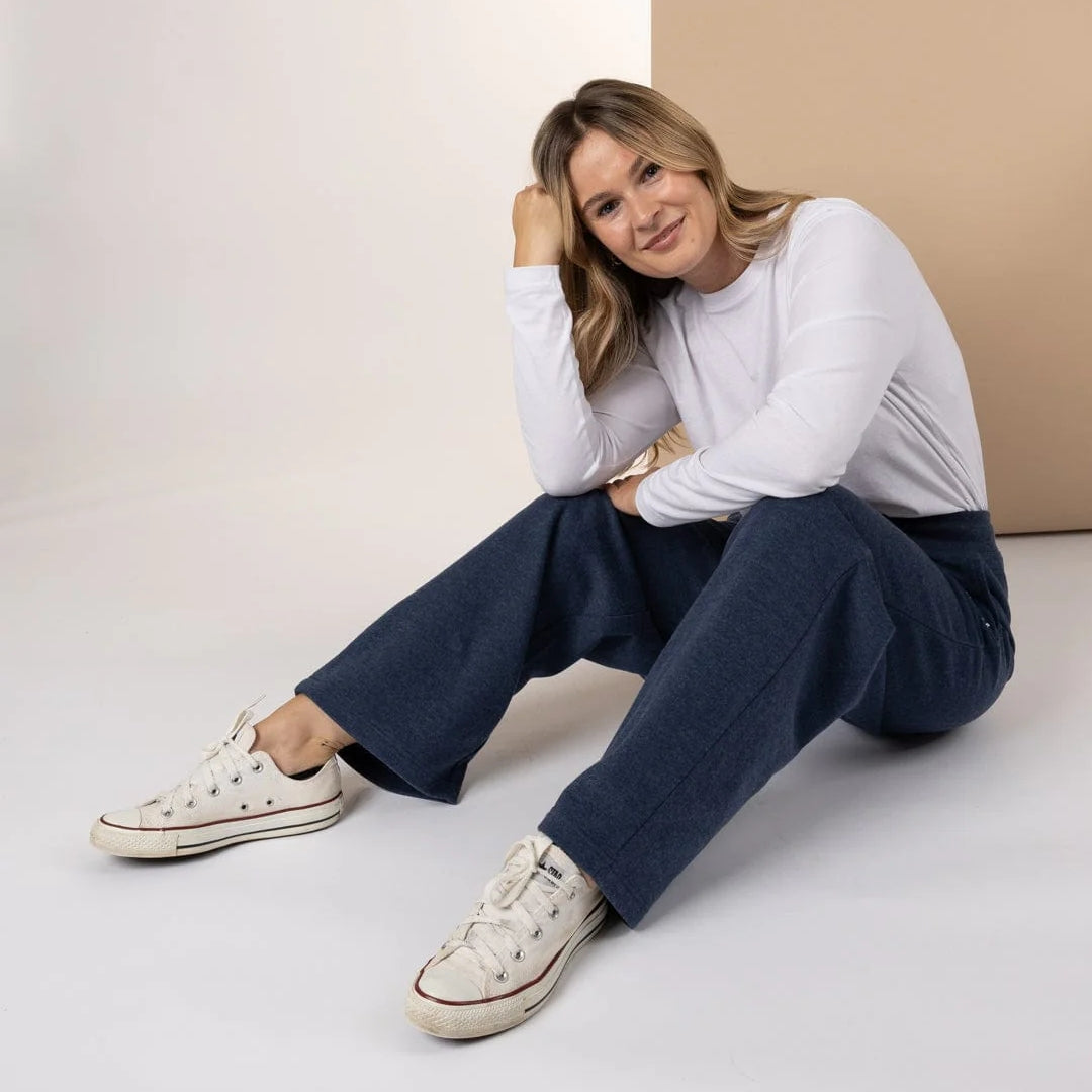 A woman sitting on the floor wearing a white long-sleeve shirt and Saltrock Velator sweat trousers in Blue Marl with white sneakers.