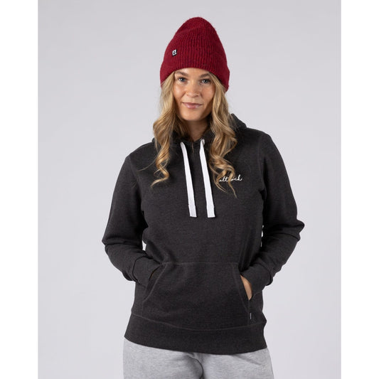 Front view of a woman wearing a dark grey Saltrock Golden Hour pop hoodie with white drawstrings and a red beanie on a light grey background