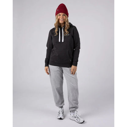 Woman wearing a dark grey Saltrock pop hoodie, grey joggers, and a red beanie on a light grey background