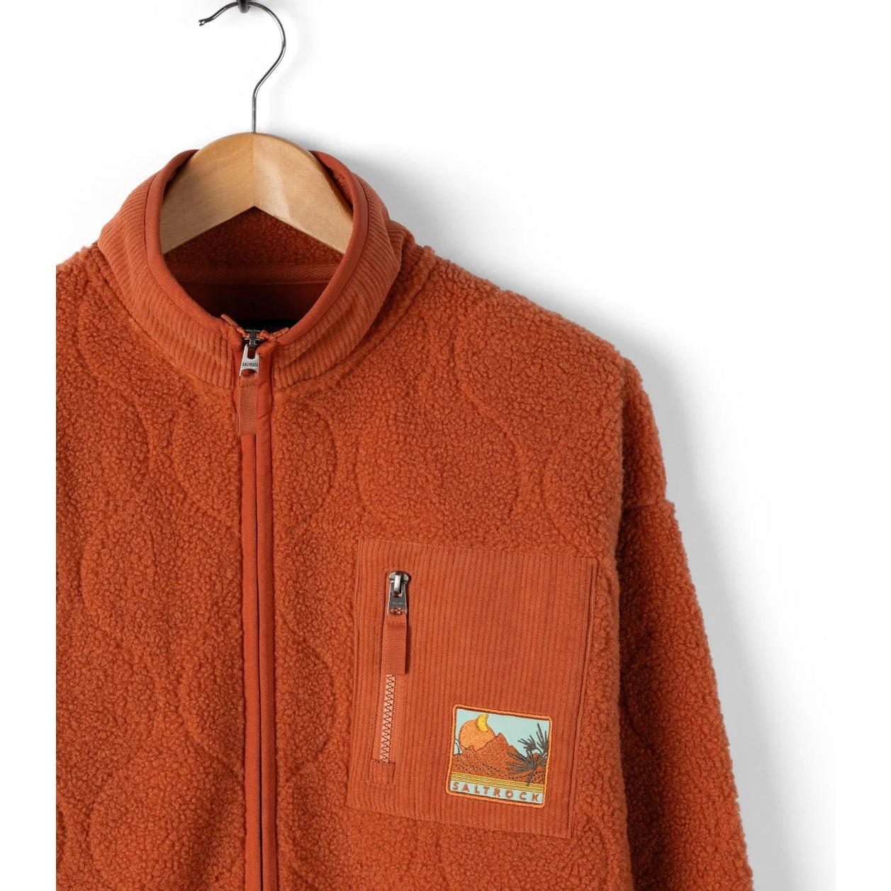 Orange fleece jacket with a patch on a hanger against a white background