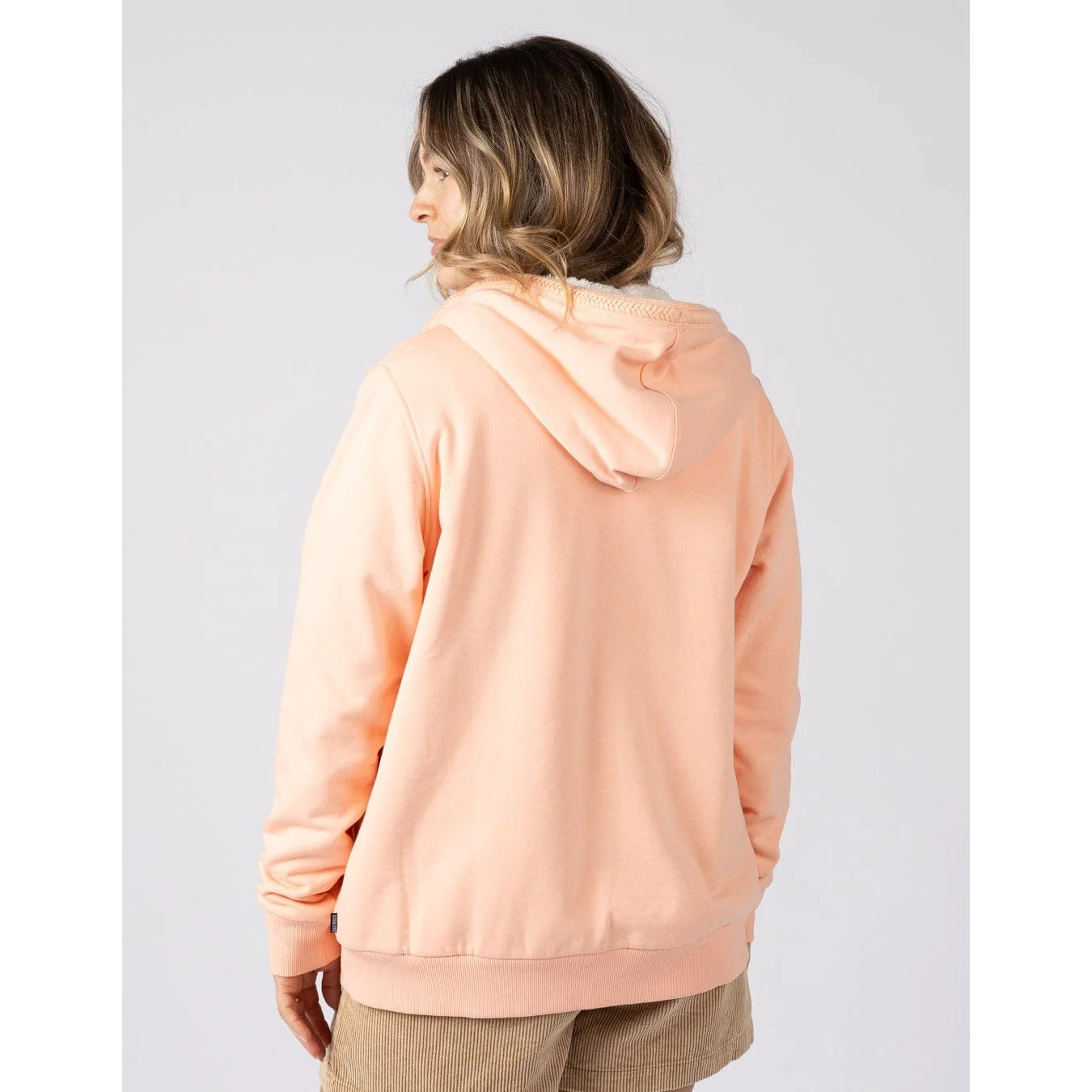 Baack view of a woman wearing a peach or light pink coloured Tamsin hoodie on a plain background