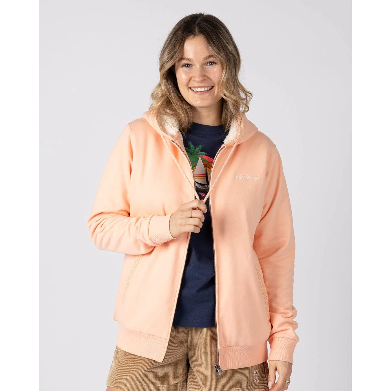 Front view of a woman wearing a peach or light pink coloured Saltrock Tamsin hoodie with white fur lining on a plain background