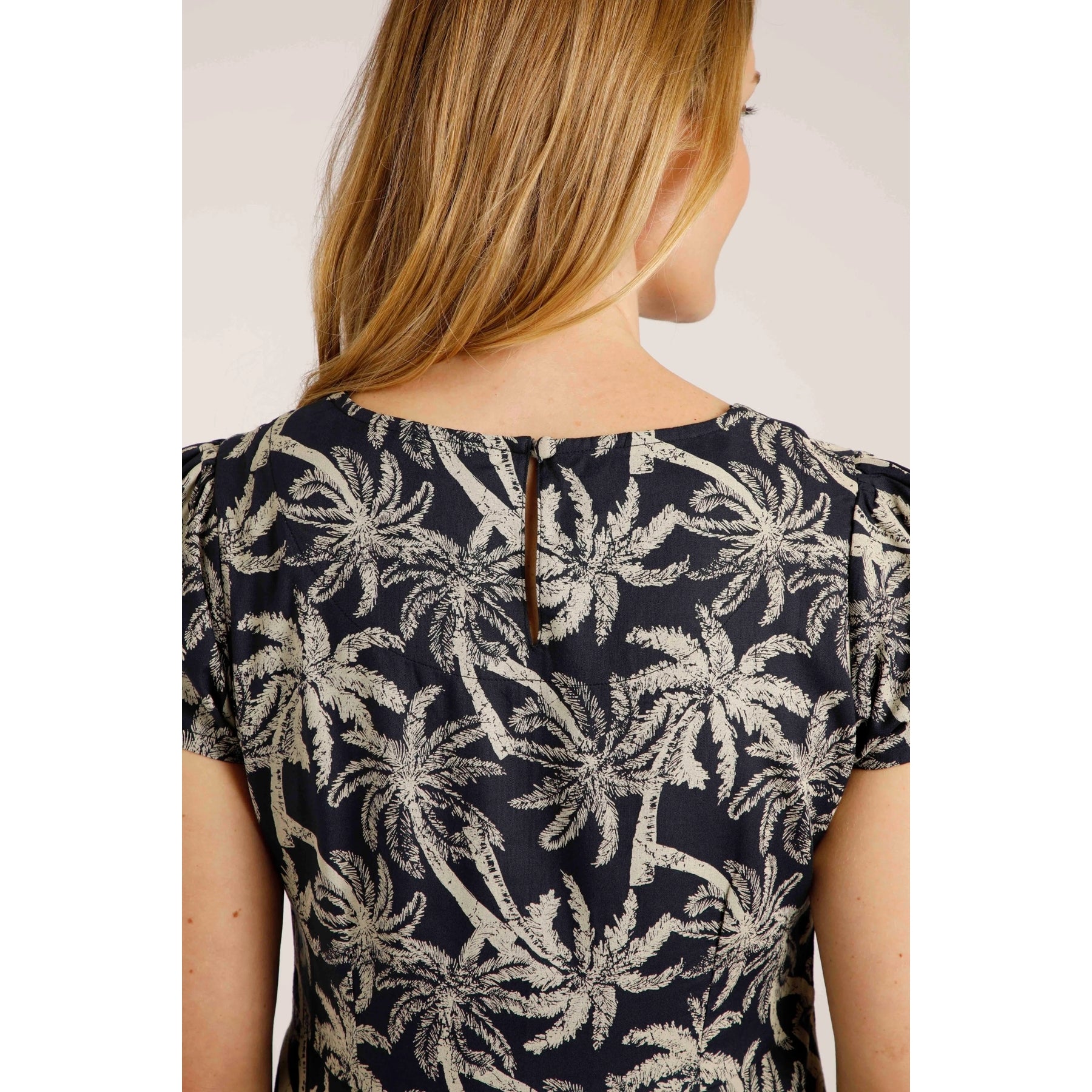 Close-up view of the back of a woman wearing a Weird Fish short sleeve Breeza tunic in Midnight Navy with a beige palm tree pattern.