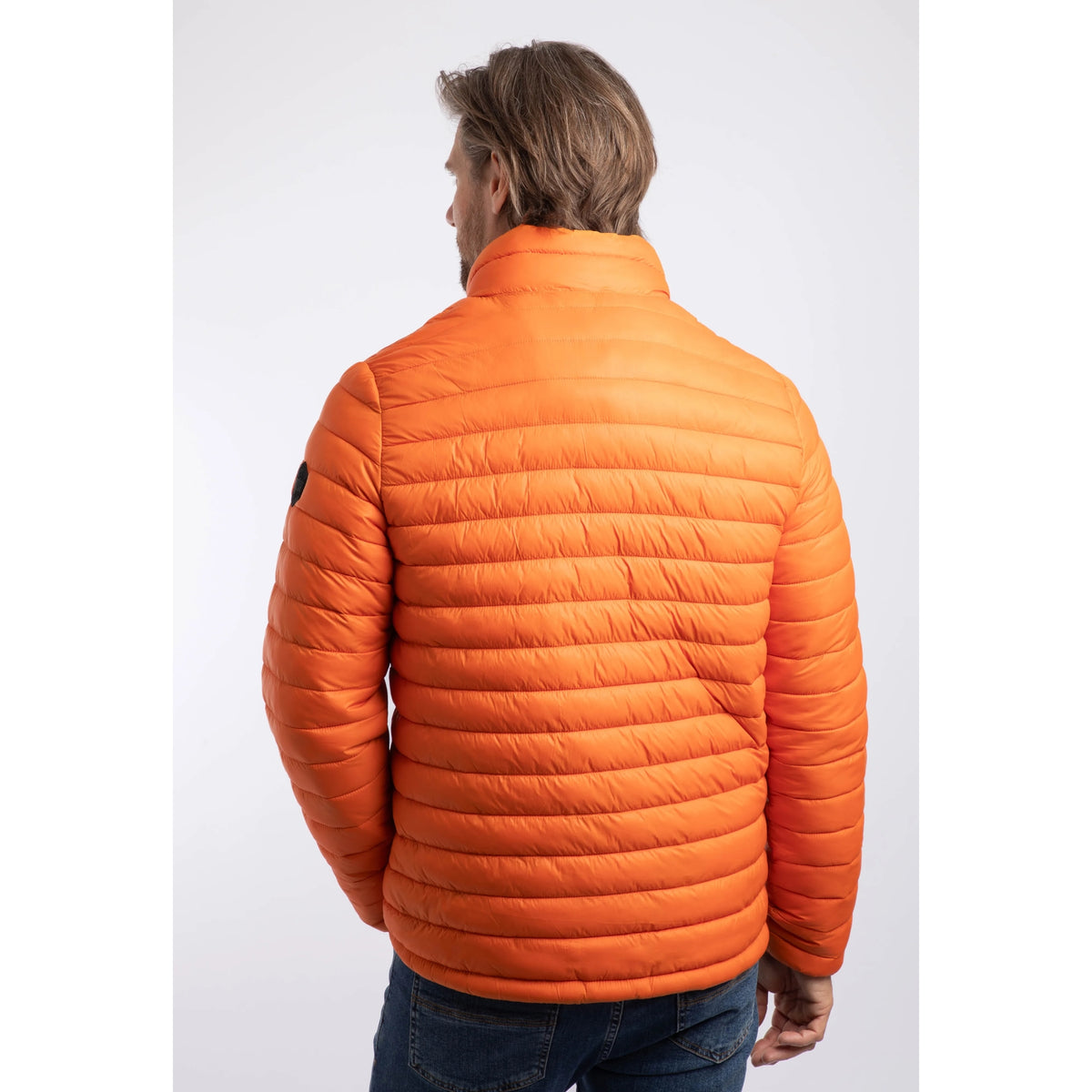 Back view of a man wearing a Weird Fish Crantock padded lightweight showerproof jacket in bright Koi Orange.