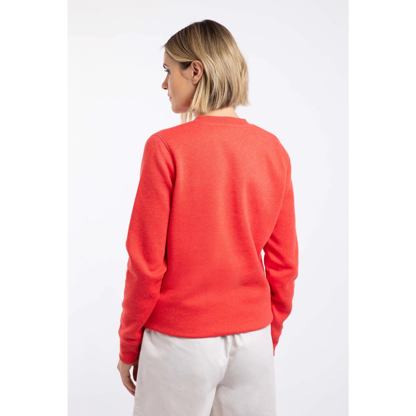 Back view of a woman wearing a Weird Fish Aurora crew neck sweatshirt in a bright coral colour with bold circular logo  print on the front.